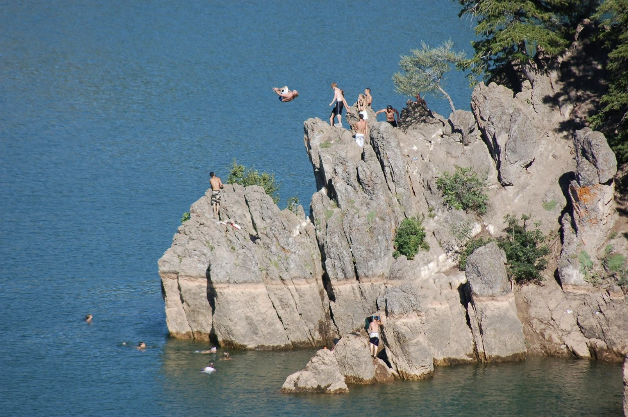 man jumping off of a 30 foot cliff into the lake