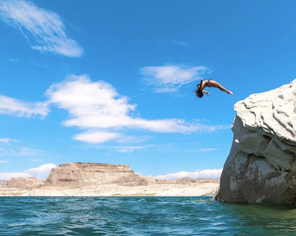 Woman diving backwards into Lake Powell with red rock in the background