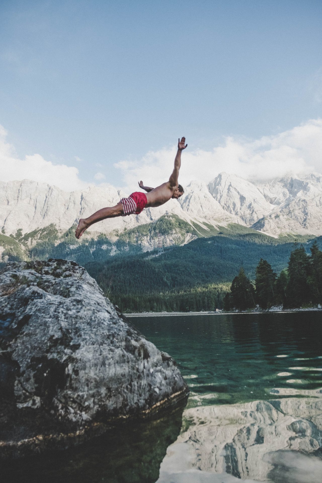 Man does a swan dive into the lake with mountains in the background