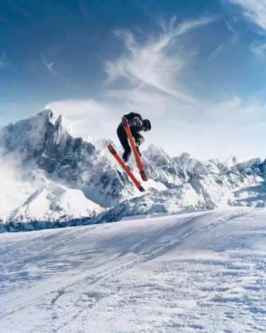 Shows man skiing by a mountain with powder in the air and clouds.