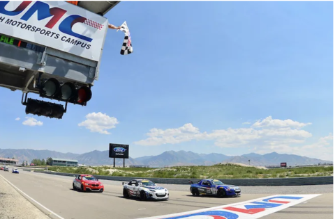 Sports cars racing across the finish line at Utah Motorsports Campus with a checkered flag waving.