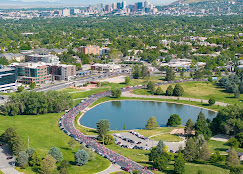 Aerial view of Sugar House Park in Salt Lake City with a large pond, green open space, walking paths, and the downtown skyline in the distance.