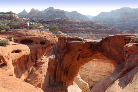 a red rock arch with red rock mountains in the distance