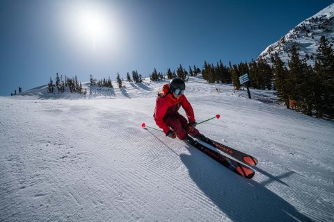 A skier in red gear carving down a groomed slope at Alta Ski Area, representing premier winter outdoor activities near Salt Lake City in the Wasatch Mountains.