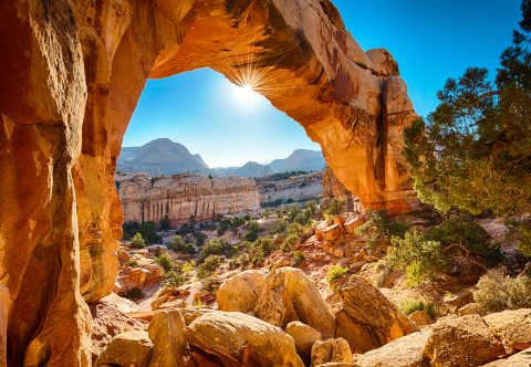 an arch with a trail underneath with sun shining and blue skies